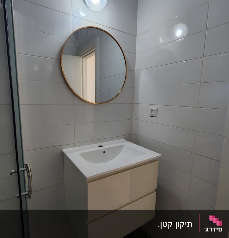 מראה עגולה, כיור לבן, ארון תלוי, קיר אריחים